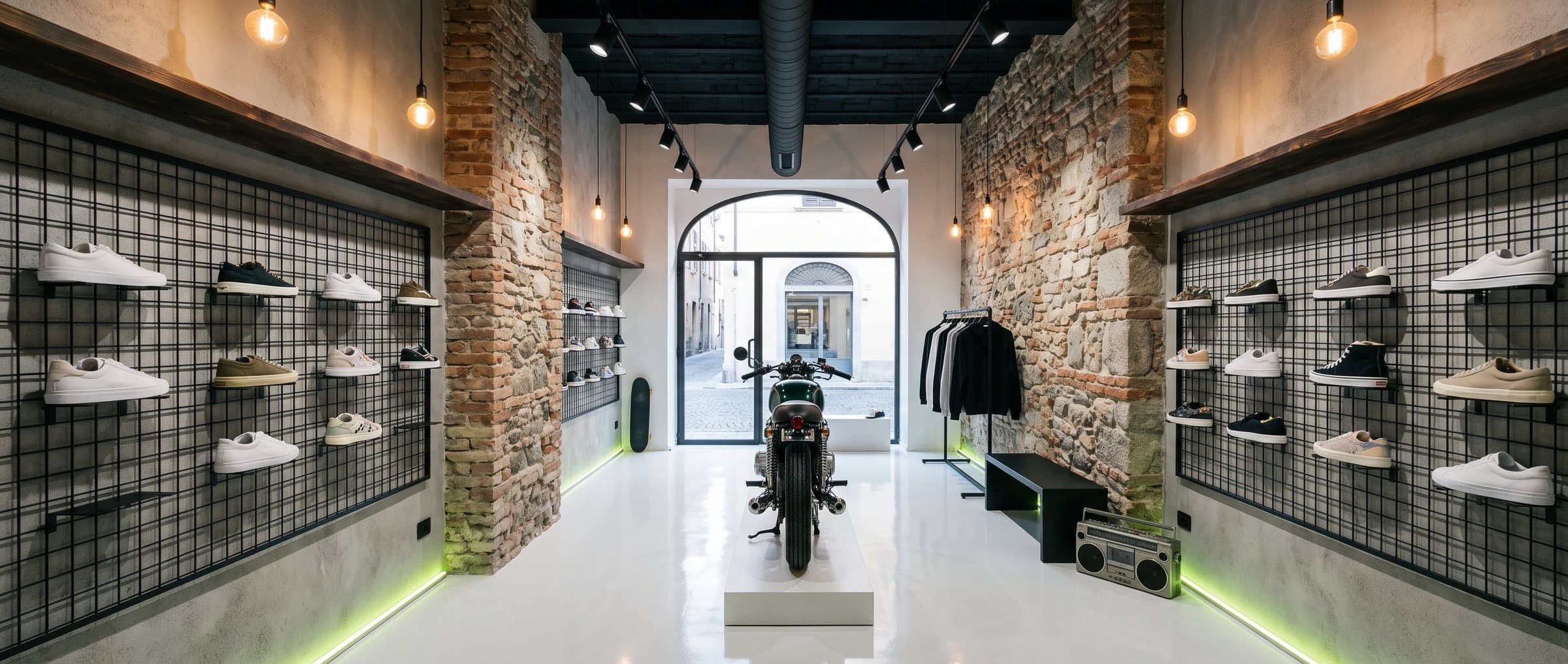 Interno del negozio Step Up a Frosinone: pareti in mattoni con griglie metalliche di sneakers e moto d'epoca al centro